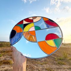 a hand holding up a colorful stained glass plate in the desert with blue sky and clouds