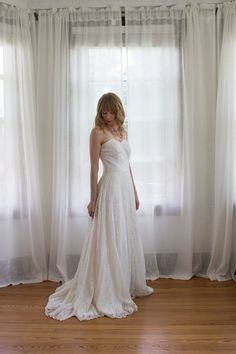 a woman standing in front of a window wearing a white dress and holding her hand to her face