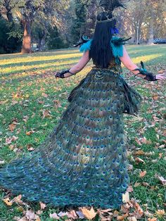 a woman in a peacock costume is walking through the grass with her hands out and two birds on her head