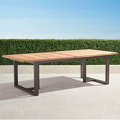 a wooden table sitting on top of a cement floor next to a green hedge covered wall