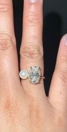 a close up of a person's hand with a diamond and pearl ring on it