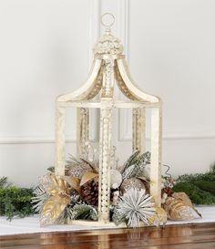 a white birdcage filled with pine cones and greenery on top of a wooden table