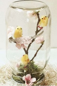 a glass jar filled with flowers and small yellow birds sitting on top of each other