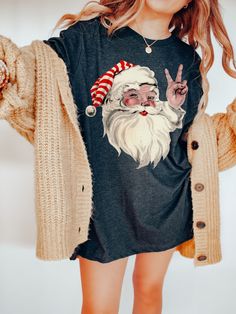 FREE SHIPPING IN THE US! Vintage Santa Shirt, Retro Christmas Shirt, Retro Santa Shirt, Santa Peace Sign Shirt, Funny Christmas Shirt, Trendy  Christmas ♥ The TEE  * This is a super soft, lightweight, comfy shirt! It is the Bella + Canvas 3001 unisex shirt.  * Many of the photos show an oversized shirt for a chic, laid back look. If you would like the shirt to be oversized like the photos, size up 1-2 sizes.   * Direct to garment printed (not vinyl). Printed in the USA. ♥ PRODUCTION & SHIPPING ＊Each shirt is made to order. ＊Production time : 2-7 business days (Excluding weekends, holidays) ＊US Shipping time : 3-7 business days ＊Most US customers received the order within 9-13 days of the order date. ＊If you have a delivery deadline or large group order, please order 14-17 days in advance. Peace Sign Shirt, Peace Sign Shirts, Retro Christmas Shirt, Retro Santa, Santa Shirt, Santa Shirts, Comfy Shirts, Funny Christmas Shirts, Vintage Santa