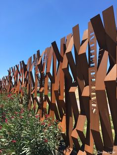 a fence made out of wooden blocks in the middle of a field with wildflowers