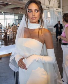 a woman wearing a white wedding dress and veil with her hands on her hips standing in front of a crowd