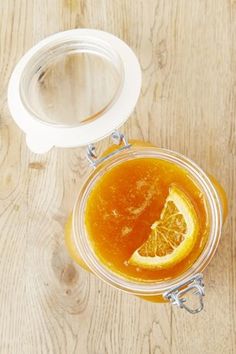 a glass jar filled with liquid sitting on top of a wooden table next to an orange slice