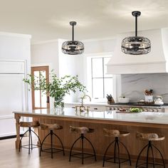 a kitchen island with stools in front of it and lights hanging from the ceiling