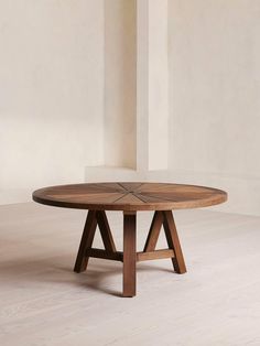 a round wooden table sitting on top of a white floor next to a tall wall