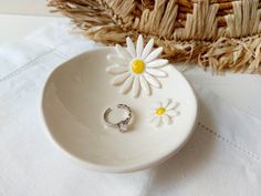 a small white bowl with two daisies on it and a ring in the middle