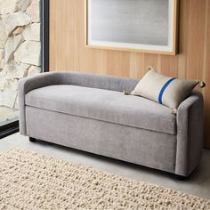 a gray couch sitting in front of a window next to a rug and painting on the wall