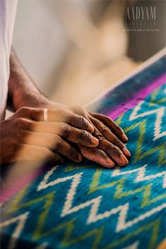 two hands on top of a colorful rug with blue and green colors in the background