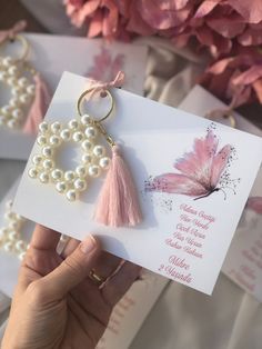 a person holding up a card with pearls and a butterfly on it, next to some flowers