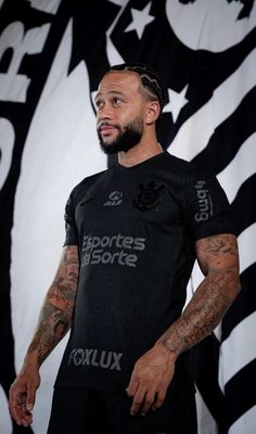 a man with tattoos standing in front of a black and white wall wearing a t - shirt