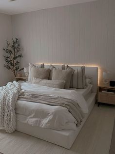 a large bed with white sheets and pillows in a bedroom next to a lamp on the wall