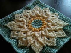 a crocheted square with a yellow and green flower on it sitting on a table