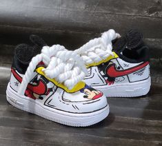 a pair of white sneakers with mickey mouse on the side and red, yellow, and black shoes