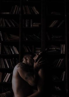 a shirtless man leaning against a bookshelf in front of a bookcase