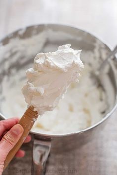 a hand holding a spoon with whipped cream on it in a metal bowl next to a spatula