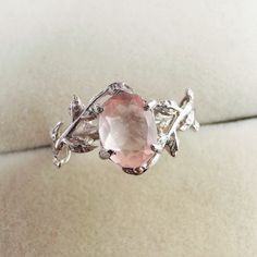 a ring with an oval pink stone surrounded by leaves and branches on a white background