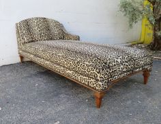 a leopard print chaise lounge sitting in front of a white wall with a tree