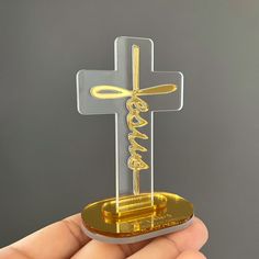 a hand holding a small cross with the word jesus in gold on it's side