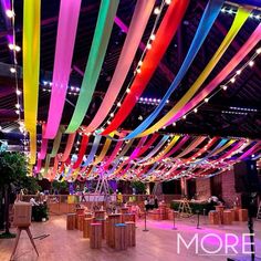 an indoor event with colorful ribbons hanging from the ceiling and tables in front of them