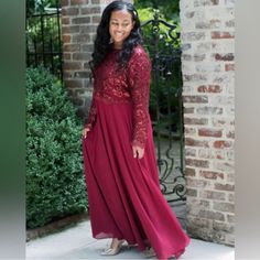 a woman standing in front of a brick wall wearing a long red dress and smiling