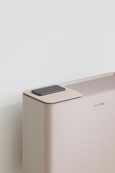 an electronic device sitting on top of a white wall next to a plant in a vase