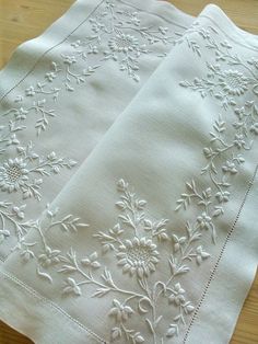 two white embroidered napkins sitting on top of a wooden table