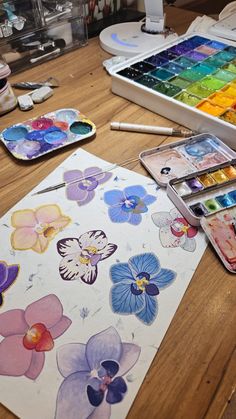 an artist's desk with watercolors, paintbrushes and flowers on it