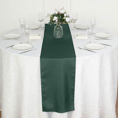 the table is set with white plates and green napkins on it, along with a vase filled with flowers