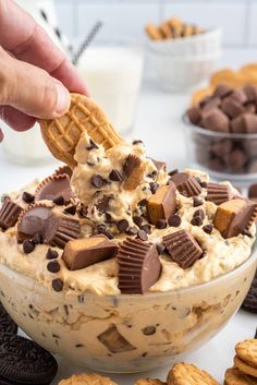 a hand holding a cracker over a bowl of ice cream and chocolate chip cookies