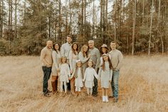 a large family is posing for a photo in the field with tall grass and trees behind them