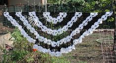 a white and black crochet shawl hanging from a wire fence in a garden