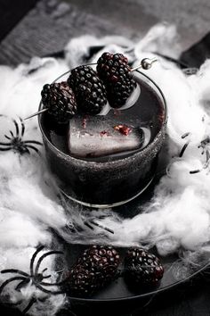 some blackberries are sitting in a glass bowl on top of cotton floss and spider webs