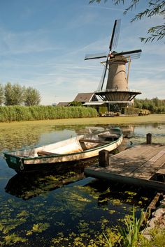 a small boat sitting on top of a lake next to a wooden dock with a windmill in the background