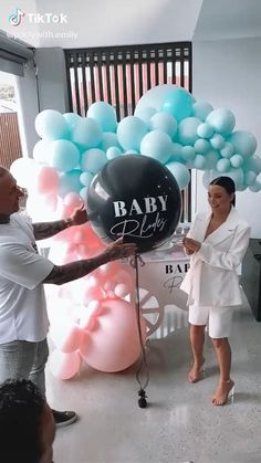 a man and woman standing next to each other in front of balloons that say baby blvd