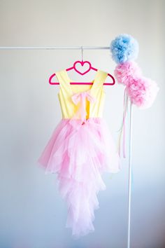 a pink and yellow dress hanging on a clothes line with a blue pom - pom