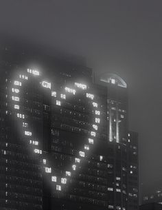 a large heart shaped building lit up in the night sky with buildings and lights behind it