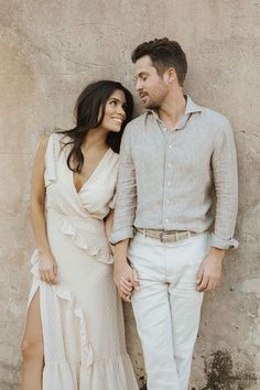 a man and woman standing next to each other near a stone wall with their arms around each other