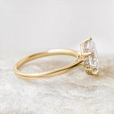 a yellow gold ring with an oval cut diamond surrounded by smaller round diamonds on a marble surface