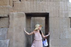 a woman in a pink dress and straw hat standing next to an ancient wall with writing on it