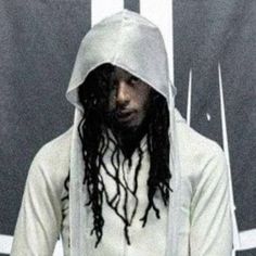 a man with dreadlocks sitting in front of a white wall wearing a hoodie