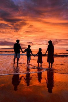 a family holding hands while standing on the beach in front of an orange and purple sunset