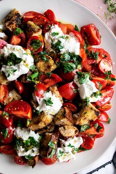 a white plate topped with tomatoes and chicken covered in feta cheese, garnished with parsley