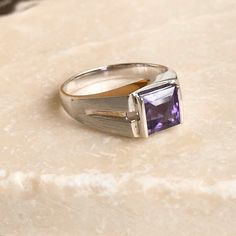 A modern style 18 carat white gold Amethyst stone ring. This beautiful piece displays a gorgeous purple stone in the clutches of a striking and bold setting. CONDITION: Wear consistent with age and use. Please see photos for more detail. STONE FACE SIZE: 6mm x 6mm APPROX. BAND WIDTH: 2mm SETTING AND STONE HEIGHT: 5mm RING SIZE: UK: M 1/2 | US: 6 1/4 WEIGHT: 4.3 grams (DZZ) Gold Amethyst Ring, Amethyst Gem, Purple Band, Cabochon Ring, Purple Stones, Gold Wedding Band, Amethyst Stone, Amethyst Ring, Stone Ring