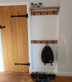 shoes are lined up in front of a wooden door with hooks on it and a backpack hanging from the wall