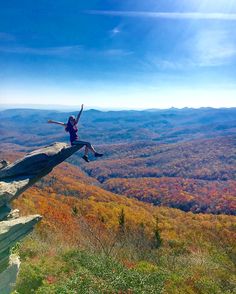 a woman sitting on top of a cliff with her arms in the air