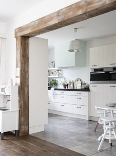 an open kitchen and dining room area with white cabinets, wood flooring and wooden beams